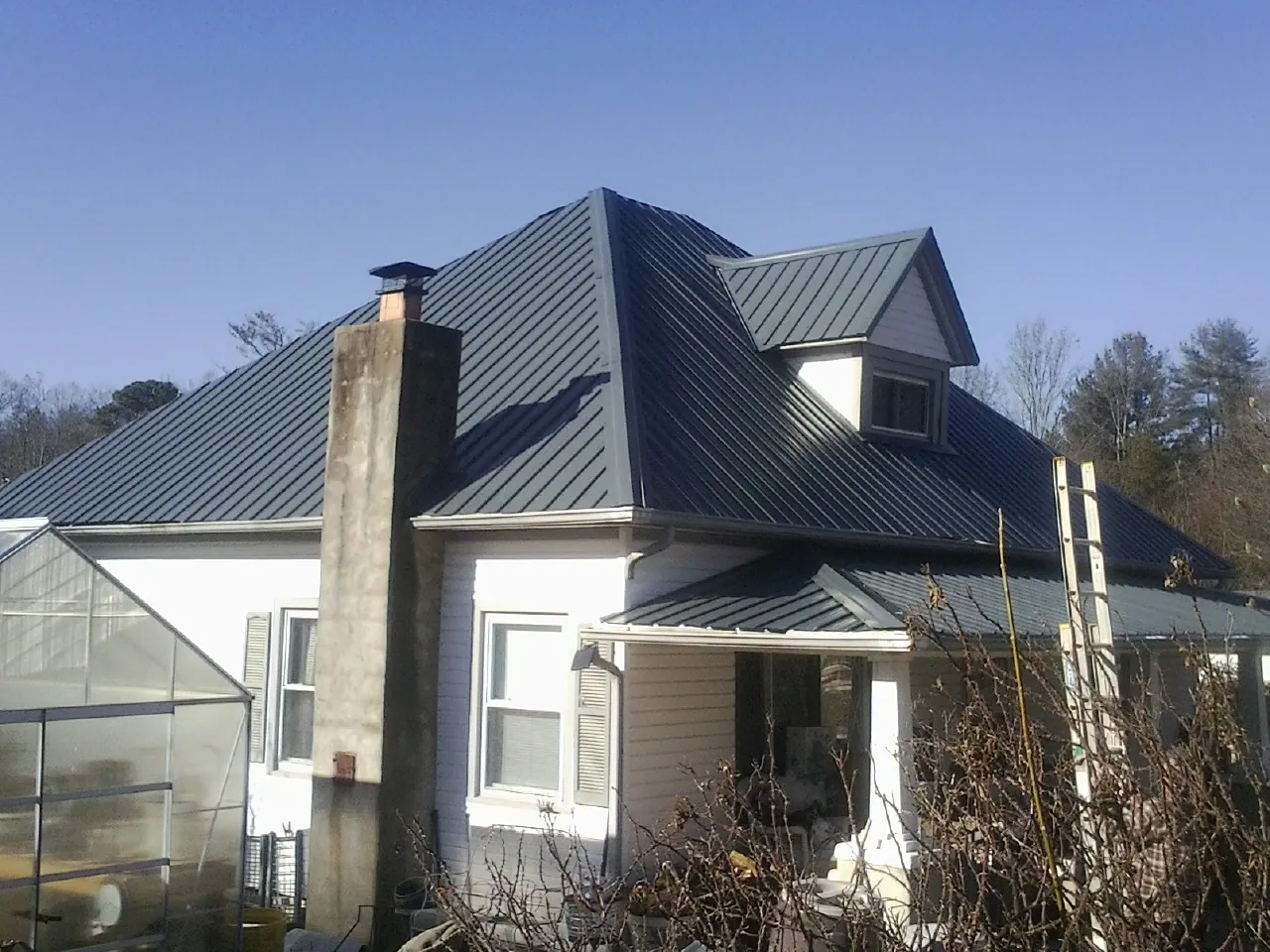 Dark blue standing seam metal roof on a white farmhouse with dormer — Slate & Tile Roof Repair by Roofing Brothers in Greenwood Springs