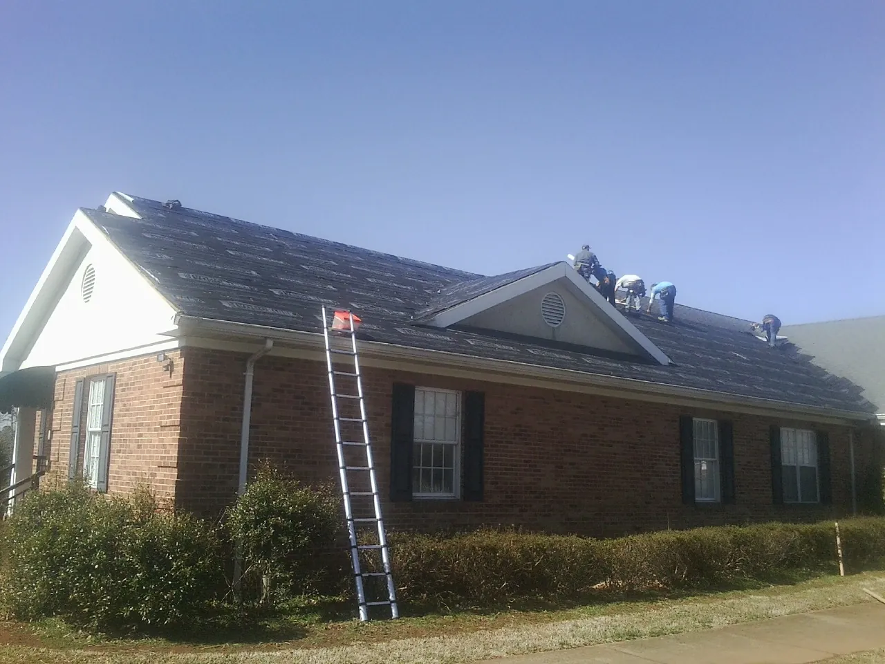 Crew tearing shingles off a brick ranch roof with a ladder set — Metal Roof Repair work by our crew in Greenwood Springs
