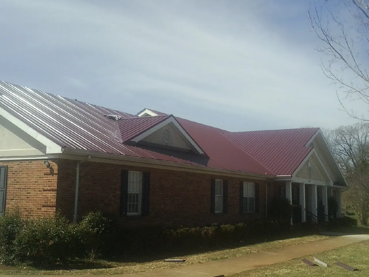 Red metal roof with gabled entries on a long brick building, from a Hail Damage Roof Repair job in Greenwood Springs