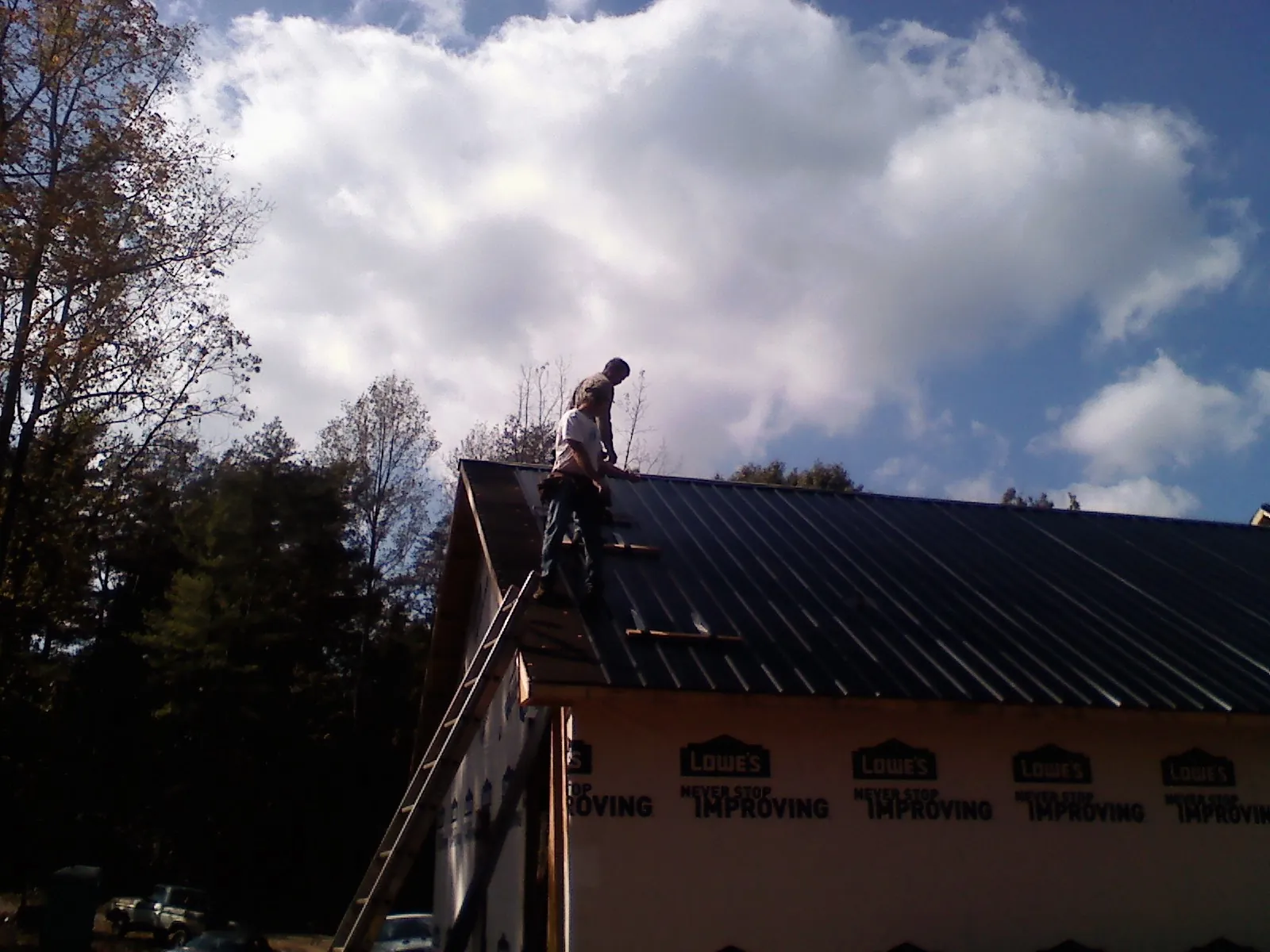 Roofer fastening dark metal panels high against a cloudy sky, from a Roof Inspection job in Greenwood Springs