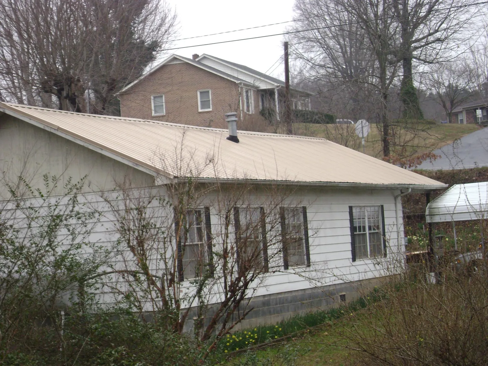 Tan metal roof on a white sided house set into a hillside — Commercial Roofing by Roofing Brothers in Greenwood Springs